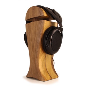 Op de afbeelding: Een houten hoofdtelefoonstandaard met een donkerbruine afwerking. De standaard is gevormd als een hoofd en heeft een groef waar de hoofdtelefoon in kan rusten. De hoofdtelefoon is zwart met een gaas oorkap.