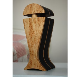 May include: A wooden decorative object with a unique design. The object is made of light wood with dark brown accents. It has a rounded top and a wide base.
