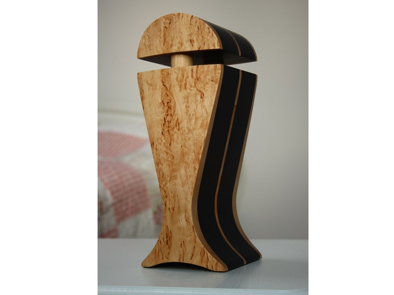 May include: A wooden decorative object with a unique design. The object is made of light wood with dark brown accents. It has a rounded top and a wide base.