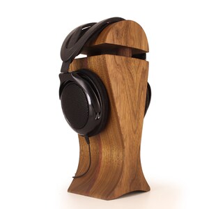 K&ouml;nnte beinhalten: Schwarze Kopfh&ouml;rer mit einem schwarzen Kabel, die auf einem Holzst&auml;nder liegen. Der St&auml;nder ist aus dunklem Holz mit nat&uuml;rlicher Maserung.