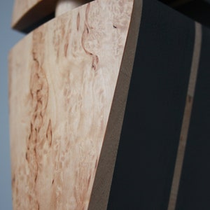 May include: Close-up of a wooden box with a black painted section. The wood has a natural, light brown color with a unique grain pattern.