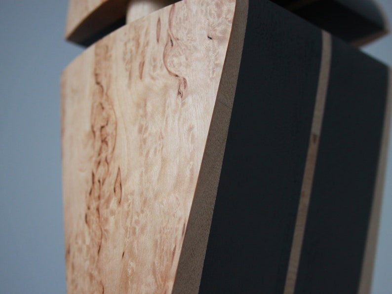 May include: Close-up of a wooden box with a black painted section. The wood has a natural, light brown color with a unique grain pattern.