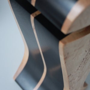 May include: Close-up of a wooden sculpture with black painted stripes. The wood has a natural grain pattern and the black paint is smooth.