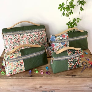 May include: Four green zippered pouches with floral fabric accents. The pouches have leather handles and are arranged in a row on a wooden surface.