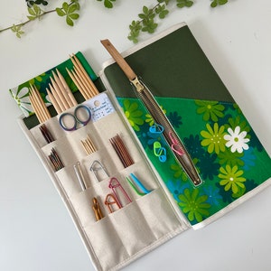Pode incluir: Um estojo de tecido para organizar agulhas de tric&ocirc; com estampa floral verde e interior creme com v&aacute;rios bolsos. Cont&eacute;m agulhas de madeira, agulhas de croch&ecirc; de metal, marcadores de pontos, uma tesoura e uma ferramenta de calibre.
