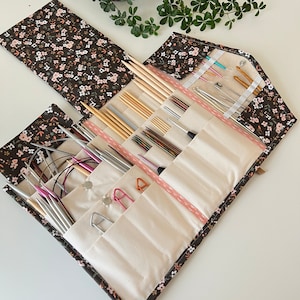 Pode incluir: Um estojo de tecido para organizar agulhas de tric&ocirc; e croch&ecirc; com uma estampa floral castanho-escura de pequenas flores cor-de-rosa e brancas. O interior &eacute; forrado com bolsos de tecido creme contendo v&aacute;rias agulhas de metal e madeira.