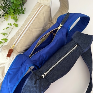 Könnte beinhalten: Drei gesteppte Umhängetaschen in verschiedenen Farben. Die obere Tasche ist beige, die mittlere Tasche ist blau und die untere Tasche ist dunkelblau. Alle drei Taschen haben Reißverschlüsse.