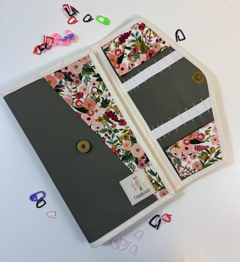 Pode incluir: Um estojo organizador de tecido cinza com padr&atilde;o floral de flores rosas, vermelhas e verdes. O estojo possui acabamento branco, fecho de press&atilde;o em lat&atilde;o e el&aacute;sticos internos. Uma pequena etiqueta branca com o texto TIANBERRY est&aacute; fixada.