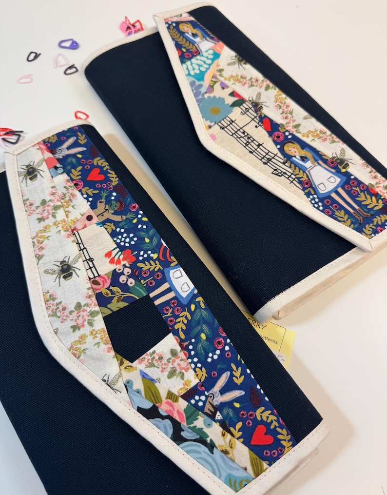 Pode incluir: Dois estojos de tecido azul-marinho com uma aba decorativa em design patchwork. O padr&atilde;o inclui ilustra&ccedil;&otilde;es de uma menina, abelhas, flores, cora&ccedil;&otilde;es e notas musicais sobre um fundo creme e azul escuro com bordas brancas.