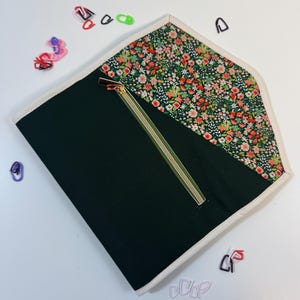 Pode incluir: Uma bolsa plana tipo envelope com corpo em tecido verde-escuro liso e aba triangular com um denso padr&atilde;o floral multicolorido. A bolsa &eacute; rematada com um debrum de cor creme e inclui um fecho de correr diagonal com um puxador met&aacute;lico.