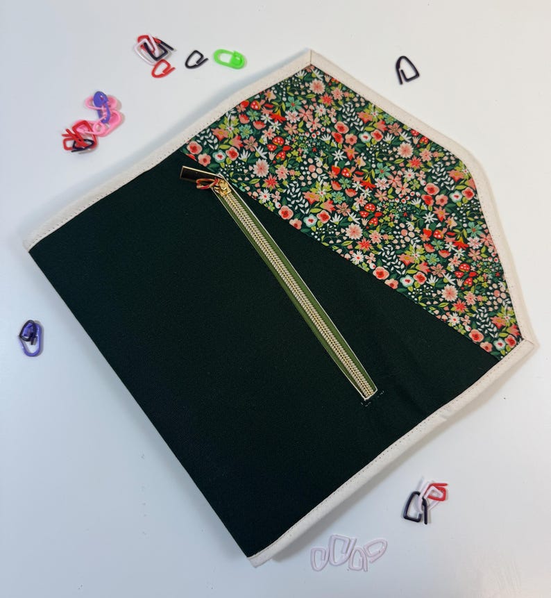 Pode incluir: Uma bolsa plana tipo envelope com corpo em tecido verde-escuro liso e aba triangular com um denso padr&atilde;o floral multicolorido. A bolsa &eacute; rematada com um debrum de cor creme e inclui um fecho de correr diagonal com um puxador met&aacute;lico.