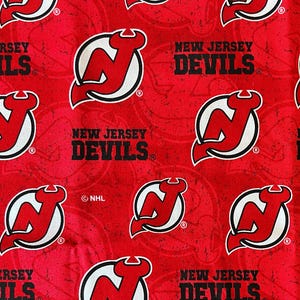 May include: Red fabric with a repeating pattern of the New Jersey Devils NHL hockey team logo. The logo is a red and white stylized 'N' with a devil's tail and horns. The fabric is printed with the words 'New Jersey Devils' in black.