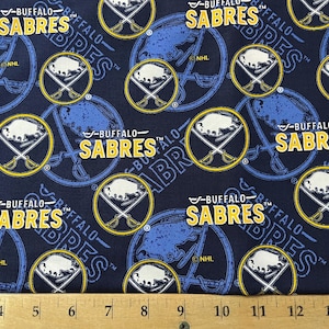 May include: Blue fabric with a repeating pattern of white buffalo heads and crossed sticks. The text "Buffalo Sabres" is repeated in yellow throughout the fabric.