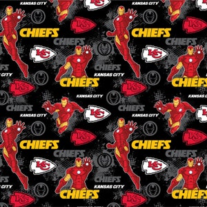 May include: A black and red fabric with a repeating pattern of a superhero in a red and gold suit, a red and white arrowhead logo, and the words "CHIEFS" and "KANSAS CITY".