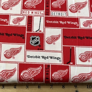 May include: Red and white fabric with a repeating pattern of the Detroit Red Wings logo, including the team name, NHL logo, and hockey stick.