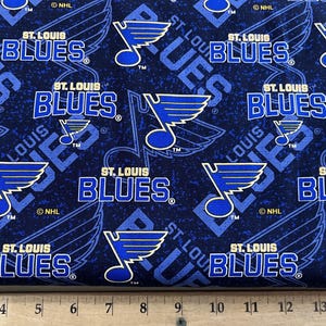 May include: Blue and white fabric with a repeating pattern of the St. Louis Blues hockey team logo. The logo features a blue note with a wing and the words "St. Louis Blues" in white.