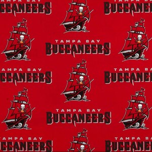 May include: Red fabric with a repeating pattern of the Tampa Bay Buccaneers logo. The logo features a pirate ship with a skull and crossbones, the words "Tampa Bay" and "Buccaneers".