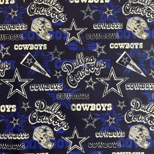 May include: A navy blue fabric with a repeating pattern of white stars, white text that says "Dallas Cowboys", and blue and white football helmets.