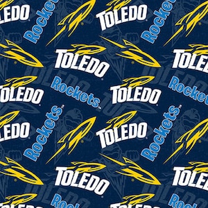 May include: Navy blue fabric with a repeating pattern of the words "TOLEDO" and "Rockets" in white and blue. Yellow rocket ship graphics are also featured. The design includes a subtle illustration of a rocket.