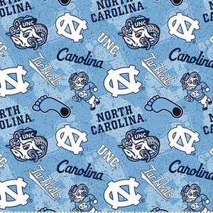 May include: A blue and white fabric pattern featuring the University of North Carolina Tar Heels logo, mascot, and team name. The pattern includes the words "Tar Heels", "Carolina", and "North Carolina".