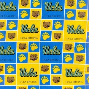 May include: A repeating pattern featuring the word "Ucla" in a stylized font, alternating with images of a bear's face and paw prints. The design is set against a blue and yellow background, with the text "UCLA BRUINS" also present.