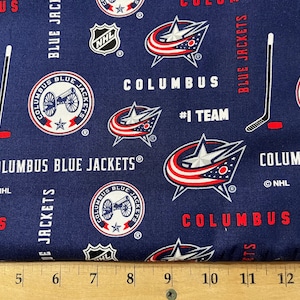 May include: Blue and red fabric with a repeating pattern of the Columbus Blue Jackets NHL hockey team logo. The logo features a star, a cannon, and the words "Columbus Blue Jackets".
