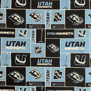 May include: A fabric with a repeating pattern of black and light blue squares. The squares feature the words "UTAH MAMMOTH" and "UTAH", along with hockey-related graphics and the NHL logo. The design is a sports-themed pattern.