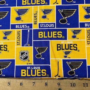 May include: A blue and yellow fabric with a repeating pattern of the St. Louis Blues hockey team logo. The logo features a blue note with a hockey stick and the words "St. Louis Blues" in white. The fabric also includes the NHL logo and the words "TM" and "®".