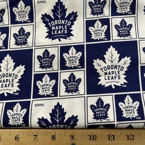 May include: White fabric with a repeating pattern of the Toronto Maple Leafs logo in blue and white. The logo features a stylized maple leaf with the words "Toronto Maple Leafs" inside. The fabric is 14 inches wide.