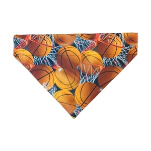 May include: A triangular dog bandana with a basketball theme. The bandana is orange, brown, and black with a pattern of basketballs and nets.