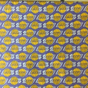 May include: Purple fabric with a repeating pattern of the Los Angeles Lakers logo. The logo is yellow and purple with a basketball in the center.