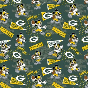 May include: A green, yellow, and black fabric with a repeating pattern of Mickey Mouse dressed as a football player, the Green Bay Packers logo, and the words "Green Bay Packers".