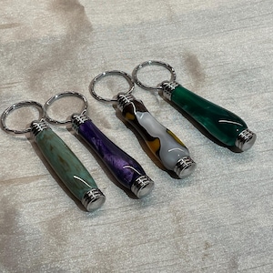 May include: Four colourful keychains with silver key rings. Each keychain has a different pattern of green, purple, white and brown.