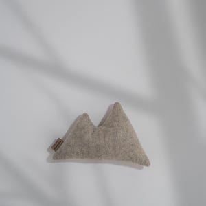 以下が含まれることがあります： 灰色のフェルトでできた山型のクッション。クッションは柔らかくふわふわで、抱きしめたり、家の装飾に遊び心を加えたりするのに最適です。