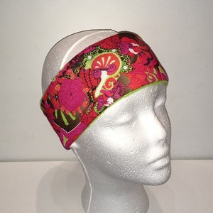 May include: A pink and green headband with a floral and abstract pattern. The headband is made of fabric and has a lime green trim.