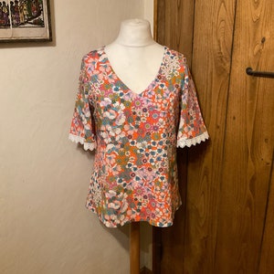 Viscose top met diepe V-hals, korte mouwen, veelkleurige bloemenprint op een oranje achtergrond.