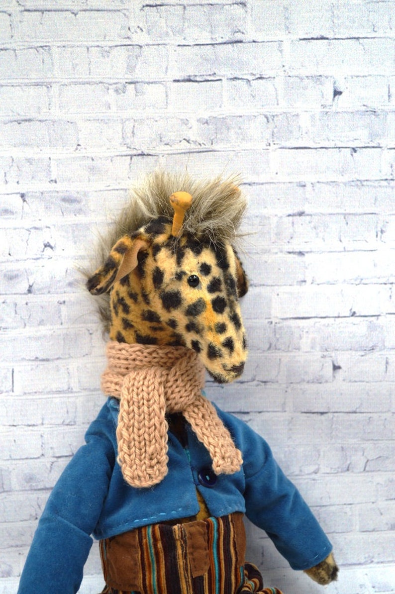 Puede incluir: Mu&ntilde;eca jirafa con cabeza manchada, melena de piel sint&eacute;tica y bufanda de punto beige. Viste una chaqueta azul y una falda marr&oacute;n a rayas. Una tee de golf de madera est&aacute; en la cabeza de la jirafa.