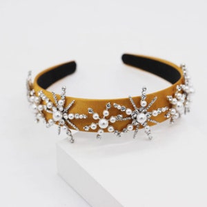 May include: A mustard yellow satin headband with silver snowflake embellishments and white pearl accents.