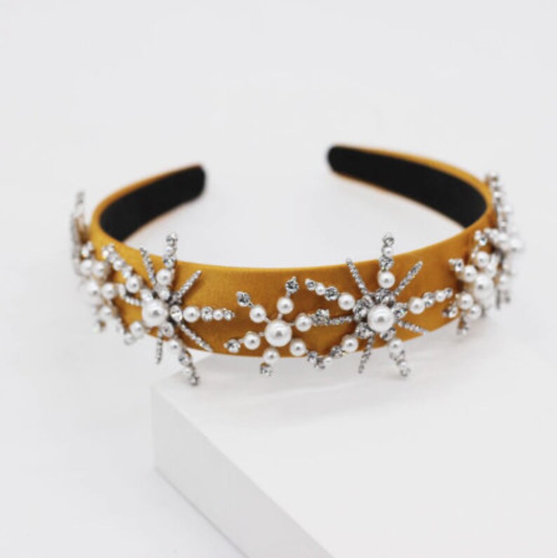 May include: A mustard yellow satin headband with silver snowflake embellishments and white pearl accents.