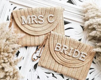 May include: Two straw clutches with white beaded lettering. One clutch says "MRS C" and the other says "BRIDE".