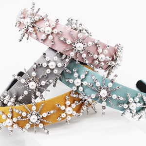 May include: Three velvet headbands with snowflake embellishments. The headbands are in pink, gray, and yellow. Each headband is decorated with silver rhinestones and white pearls.