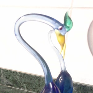 May include: A blue glass sculpture of two birds with long necks and beaks. The birds are intertwined and have a green and yellow accent on their heads.