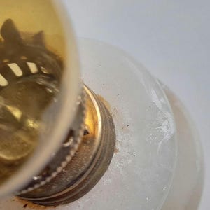 May include: Close-up of a white alabaster lamp base with a gold metal top. The lamp base has a textured surface.