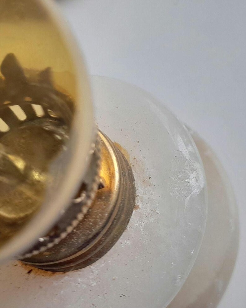 May include: Close-up of a white alabaster lamp base with a gold metal top. The lamp base has a textured surface.