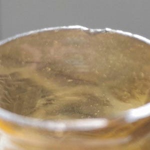 May include: Close-up of the inside of a clear glass bottle with a slightly yellowed tint. The bottle has a round opening and a smooth, slightly textured surface.
