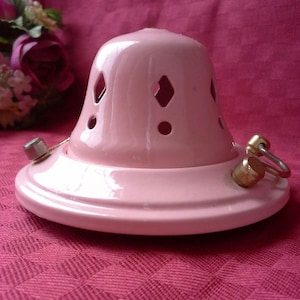 以下が含まれることがあります： ダイヤモンド型の切り抜きが施されたピンクのセラミック製ランプシェード。ランプシェードの側面には金色の金属製のリングが付いています。