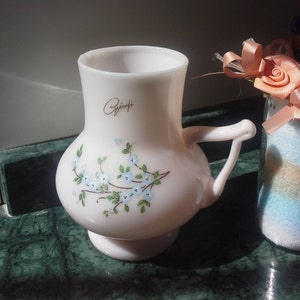 May include: A pink glass pitcher with a floral design and a handle. The pitcher has the word "Griffi" written on it.