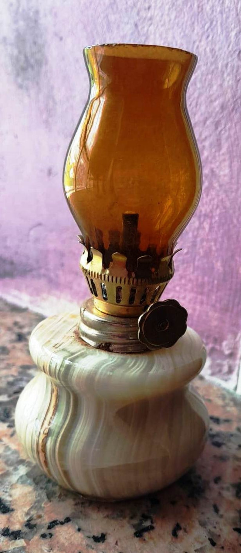 May include: A small oil lamp with a white marble base and a clear amber glass chimney. The lamp has a brass wick holder and a brass knob on the side.