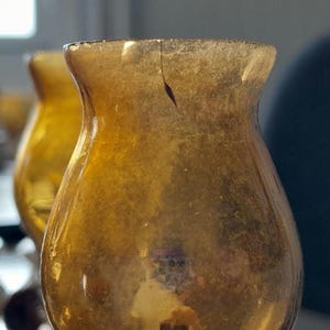 May include: A set of amber glass candle holders with a vintage look. The holders are made of thick glass and have a rounded shape.