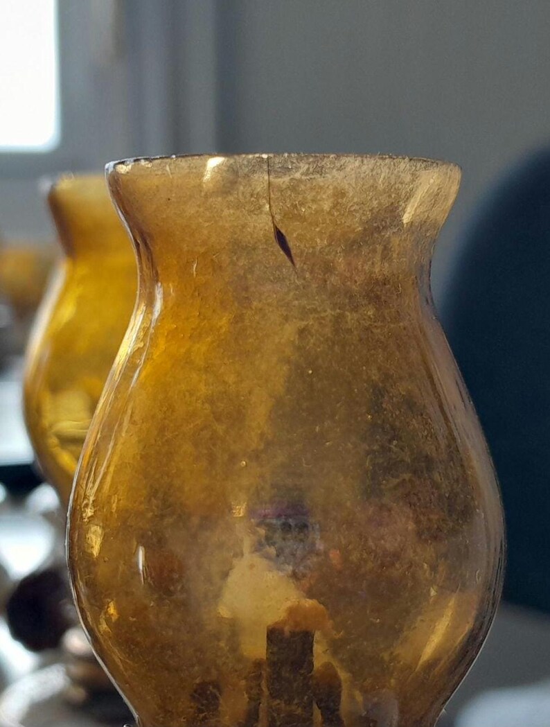 May include: A set of amber glass candle holders with a vintage look. The holders are made of thick glass and have a rounded shape.